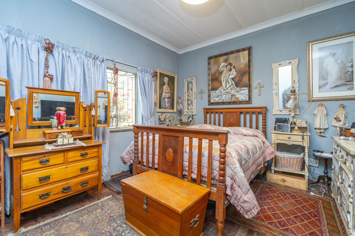 A cozy bedroom featuring traditional wooden flooring, classic cornicing, and a window with security bars.