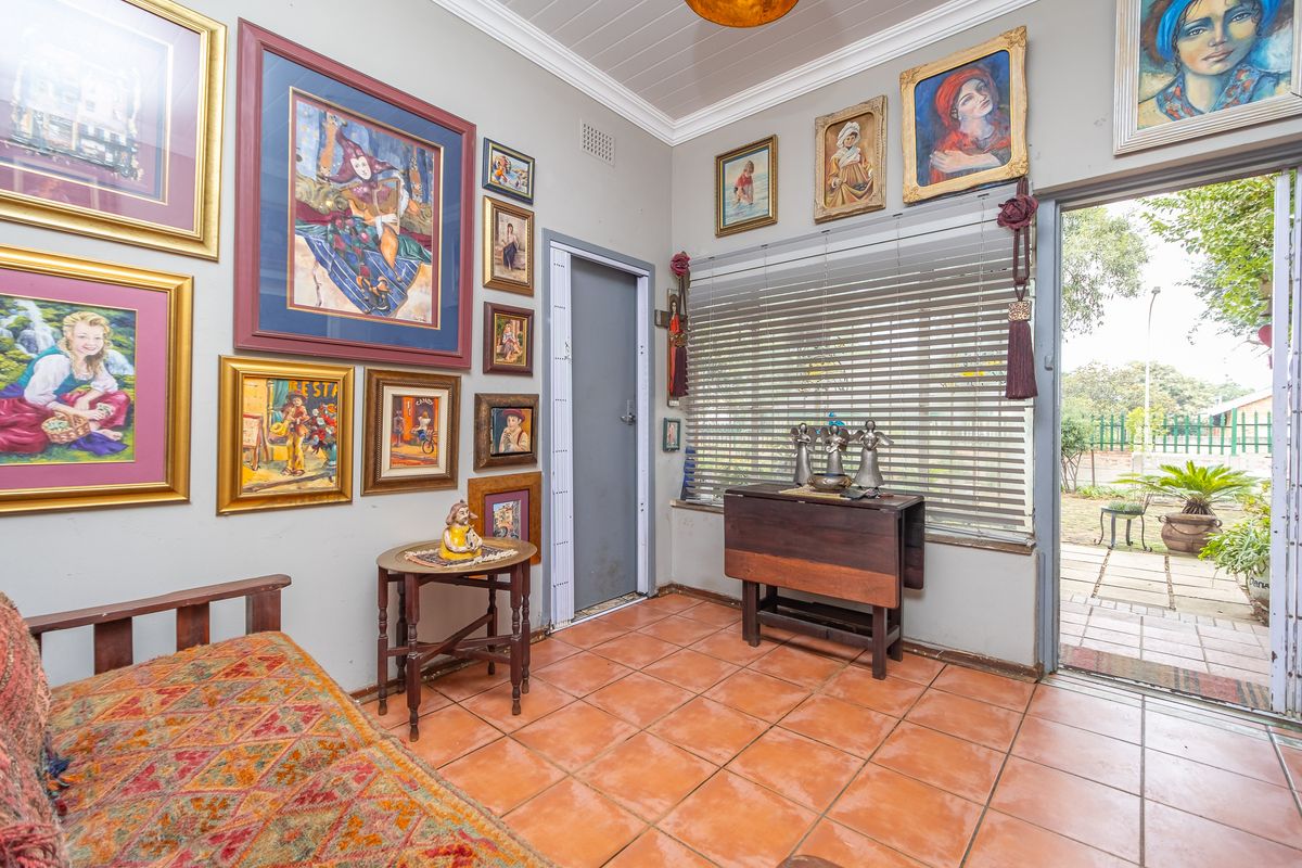 A living area featuring terracotta floor tiles, large windows with venetian blinds, and direct access to an outdoor patio area.