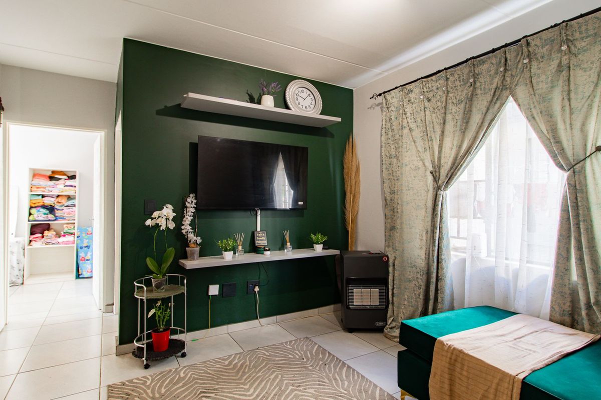A well-maintained living room featuring a bold green accent wall, tiled flooring, and a large window with natural light.