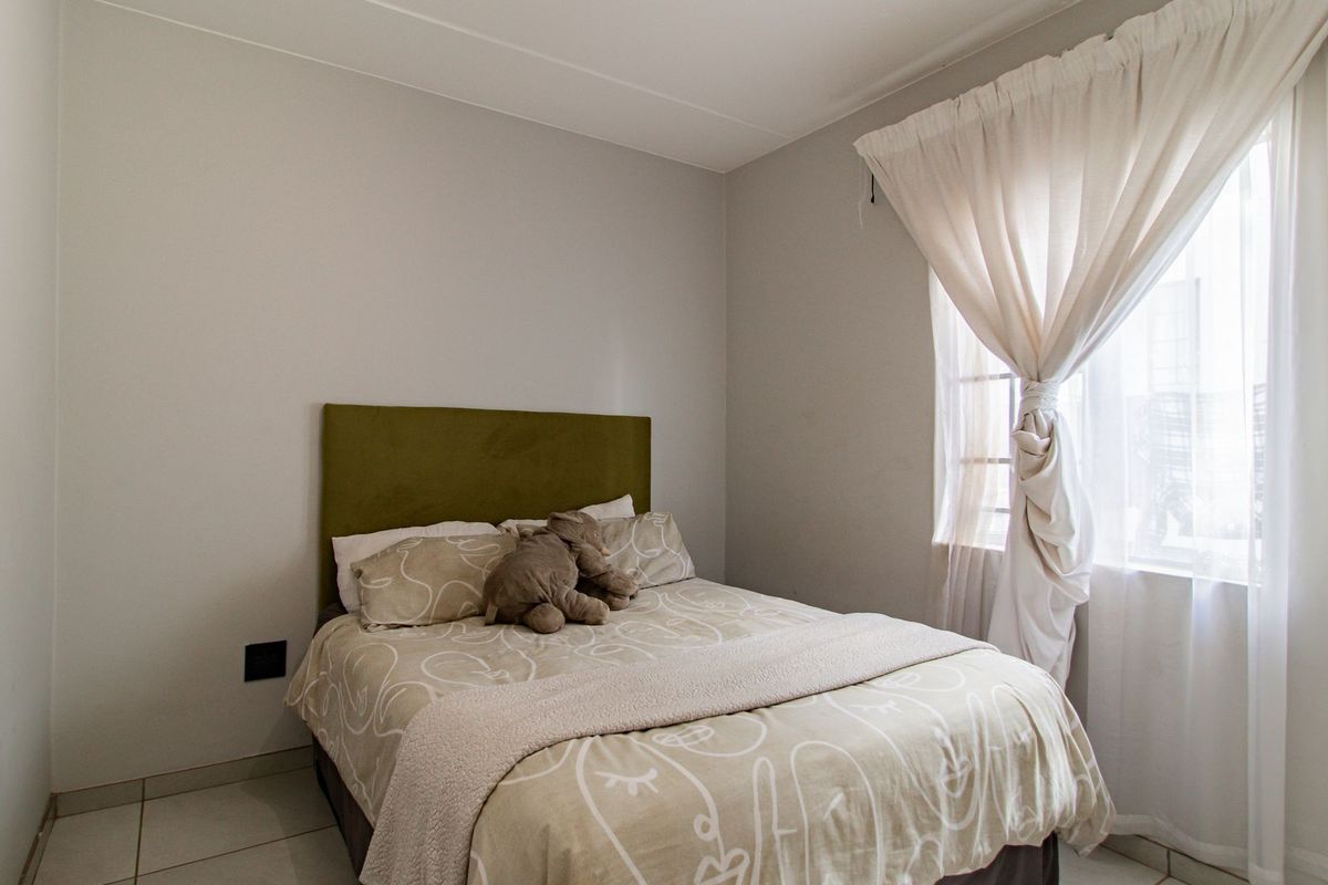 A functional bedroom featuring neutral wall tones, tiled flooring, and a window with fitted curtain tracks.