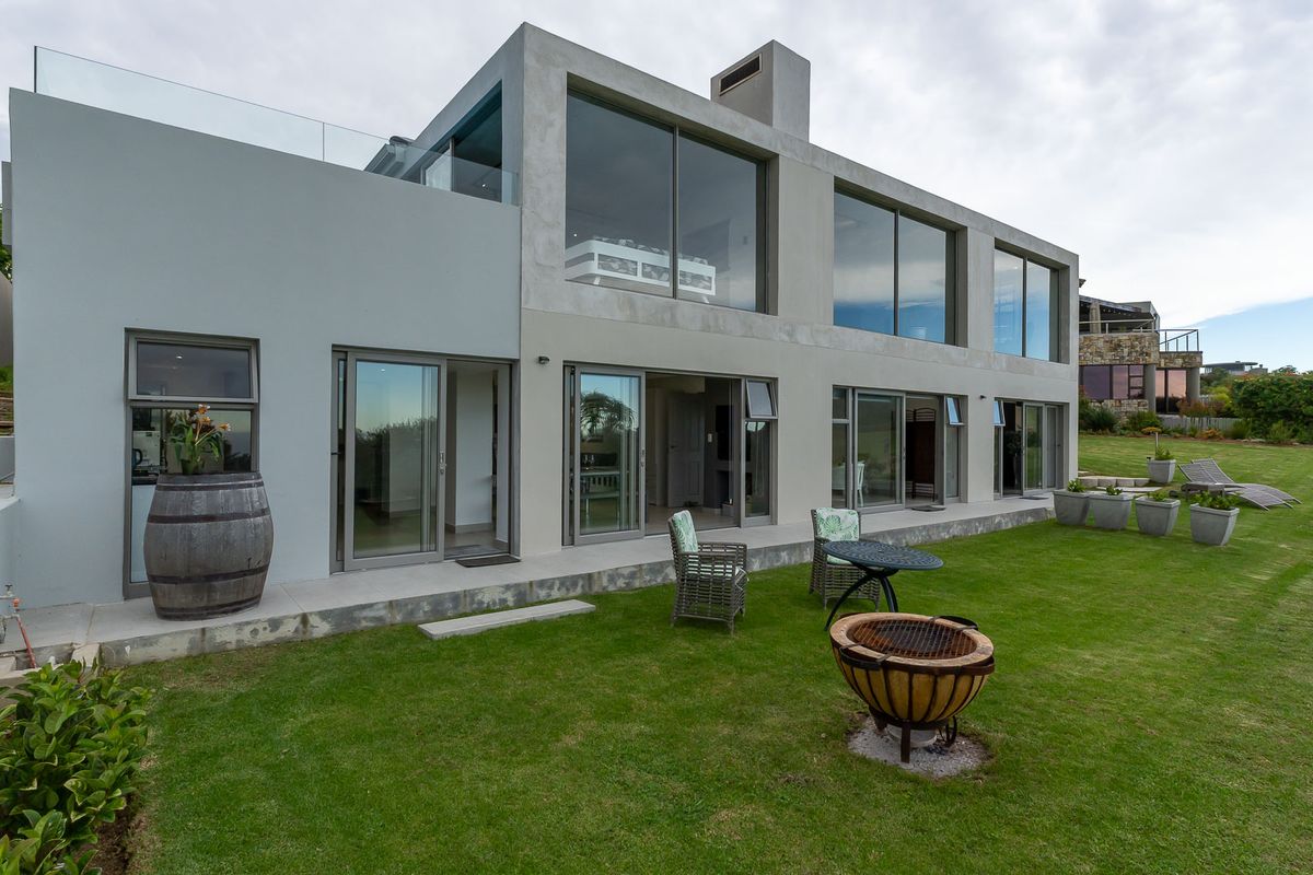 Modern two-story residential exterior featuring large glass sliding doors, concrete-style facade, and a spacious rear lawn area.
