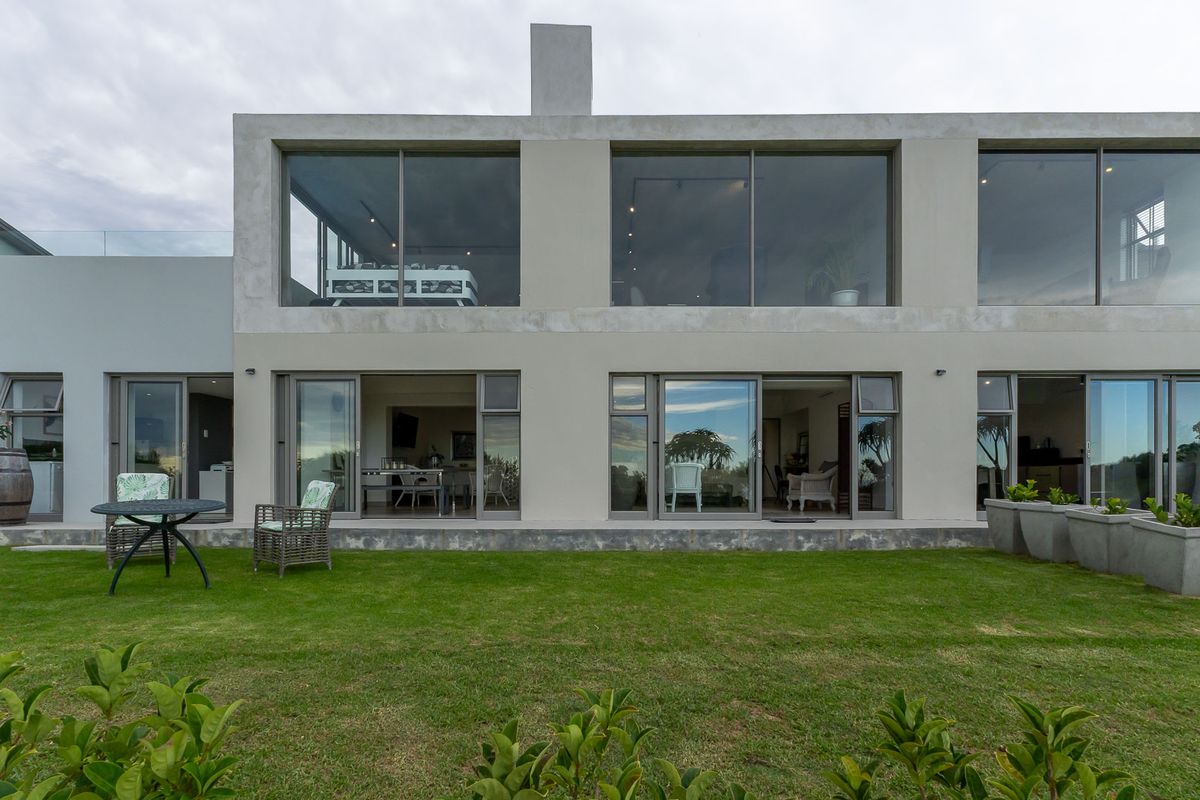 Modern two-story residential exterior featuring large glass sliding doors, expansive windows, and a well-maintained rear lawn.