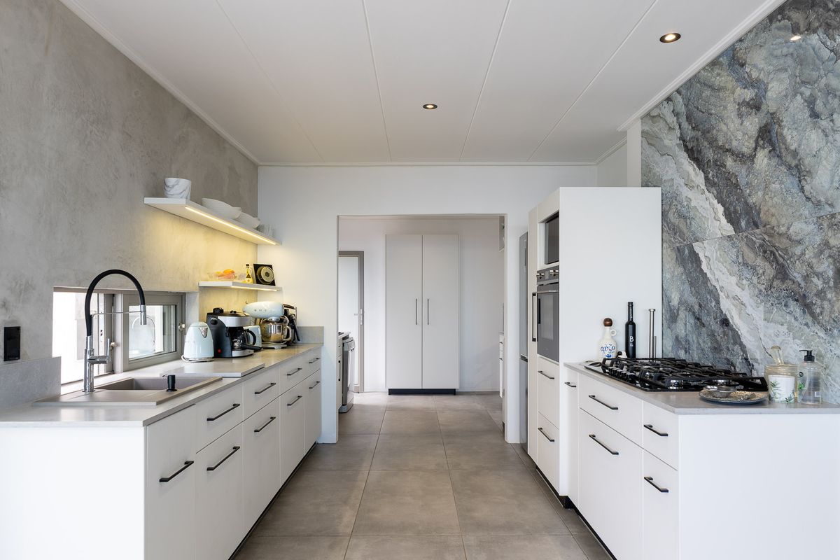 Modern galley-style kitchen featuring white cabinetry, stone-look splashback, integrated oven, gas hob, and sleek tiled flooring.