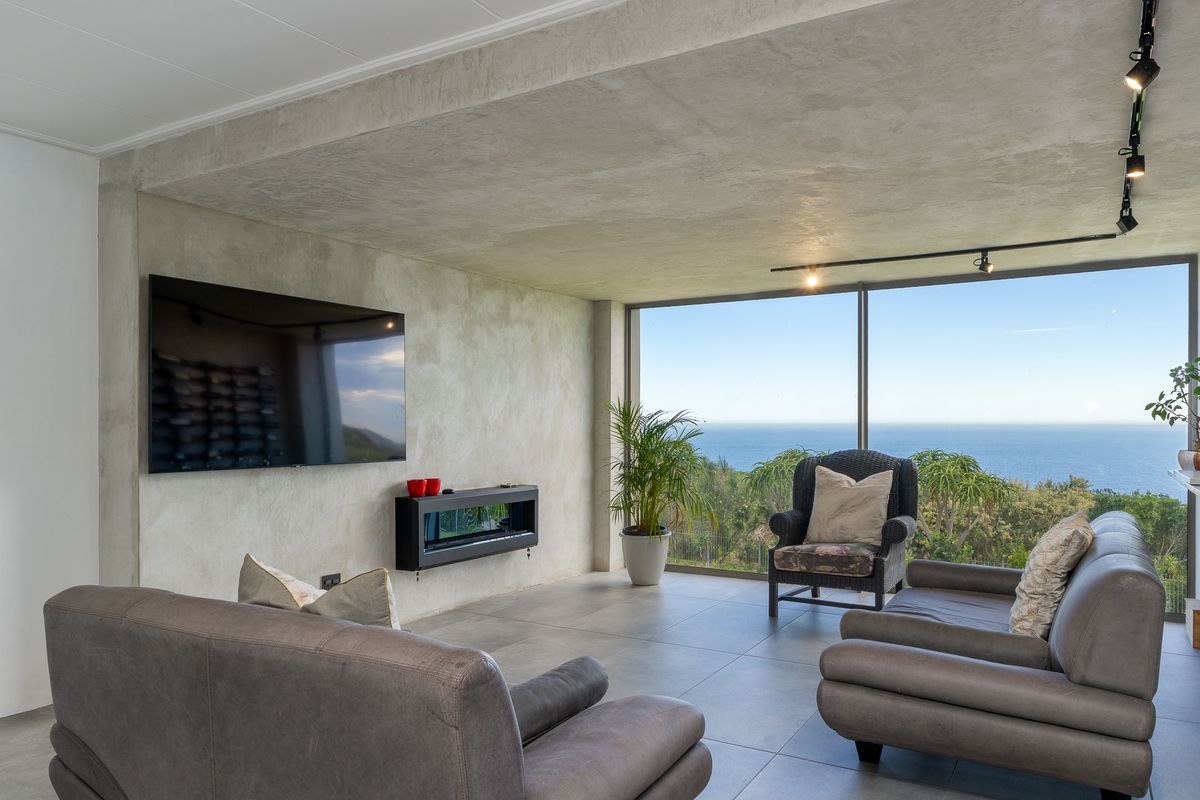 Modern living area featuring a sleek wall-mounted fireplace, large floor-to-ceiling windows, and expansive ocean views.