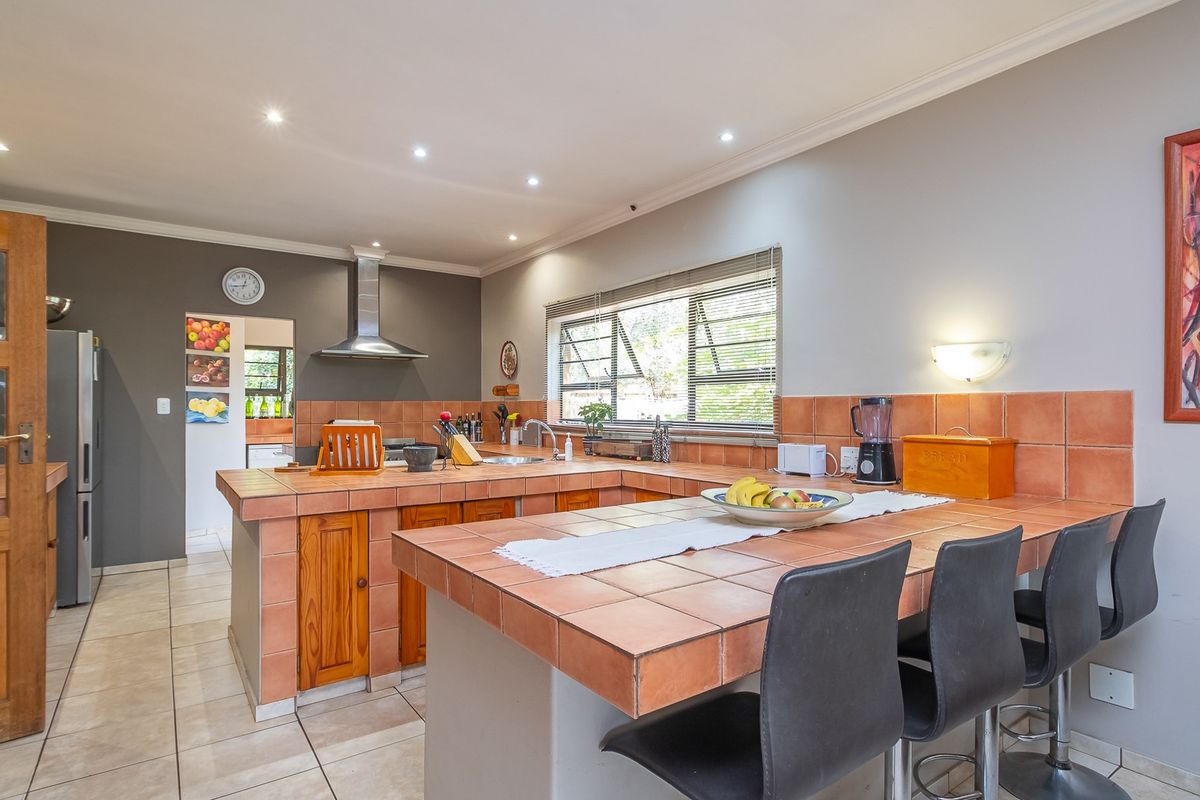 A spacious kitchen featuring tiled countertops, wooden cabinetry, a stainless steel extractor fan, and a breakfast bar area with recessed ceiling lighting.