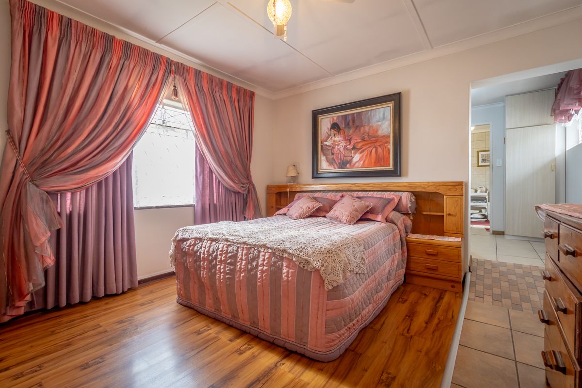 A bedroom featuring wood-look flooring, a built-in wooden headboard with integrated storage, and access to an adjoining room.