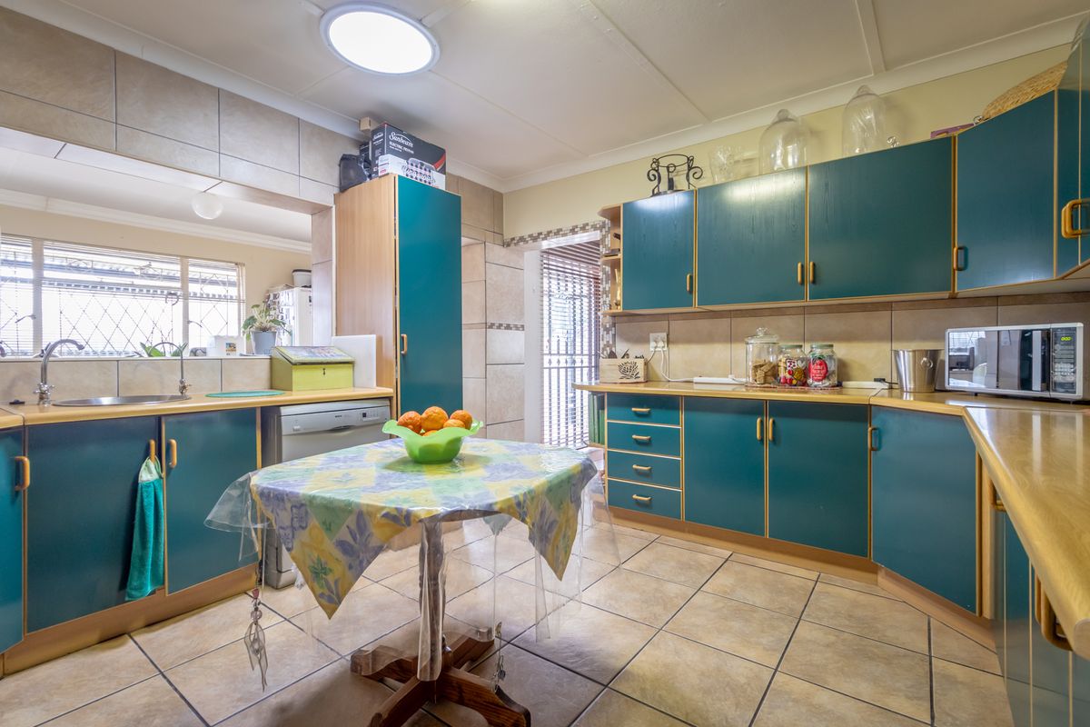 A functional kitchen featuring teal cabinetry, tiled flooring, and a pass-through window connecting to the adjacent living space.