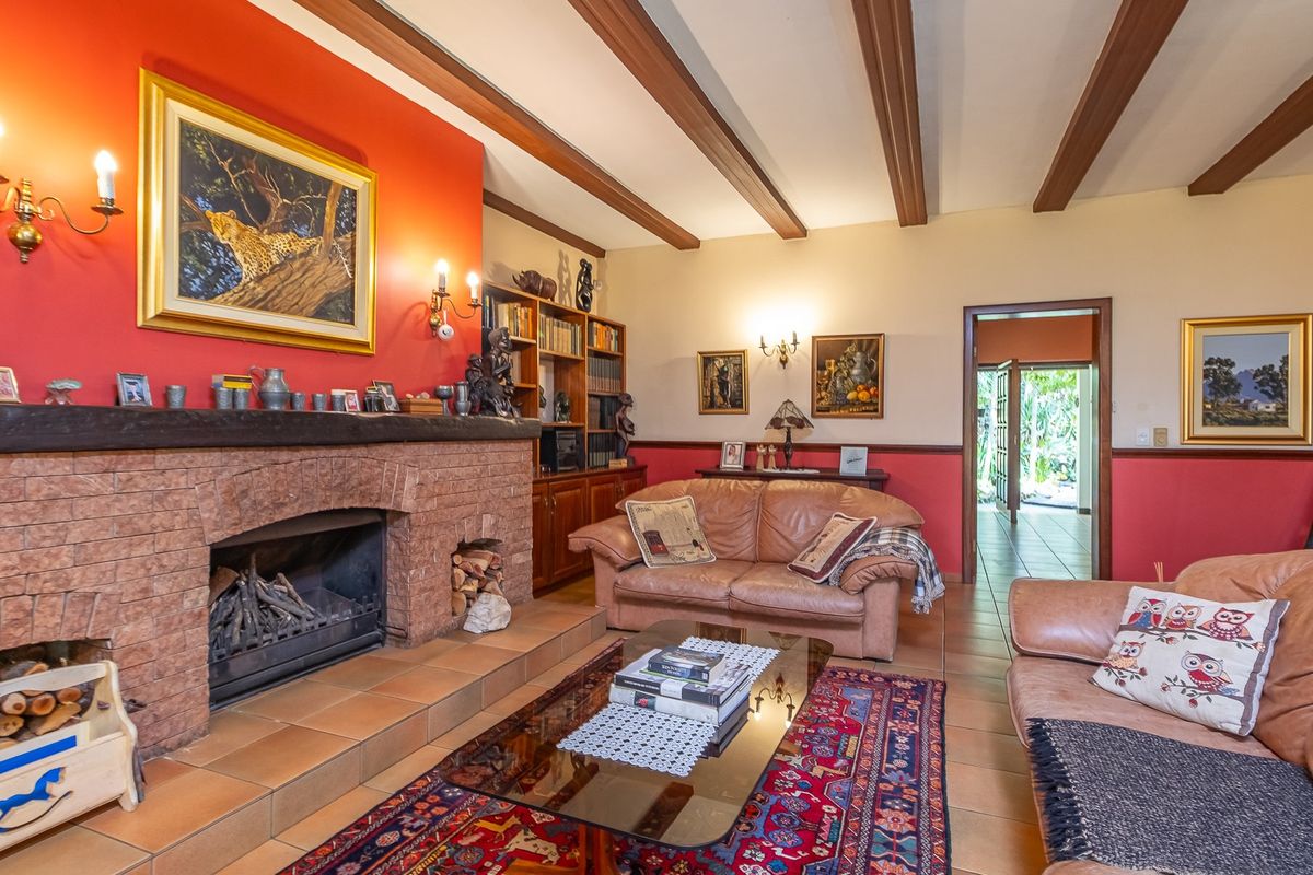 A cozy living room featuring a prominent brick fireplace, exposed timber ceiling beams, and terracotta floor tiles, creating a warm and traditional atmosphere.