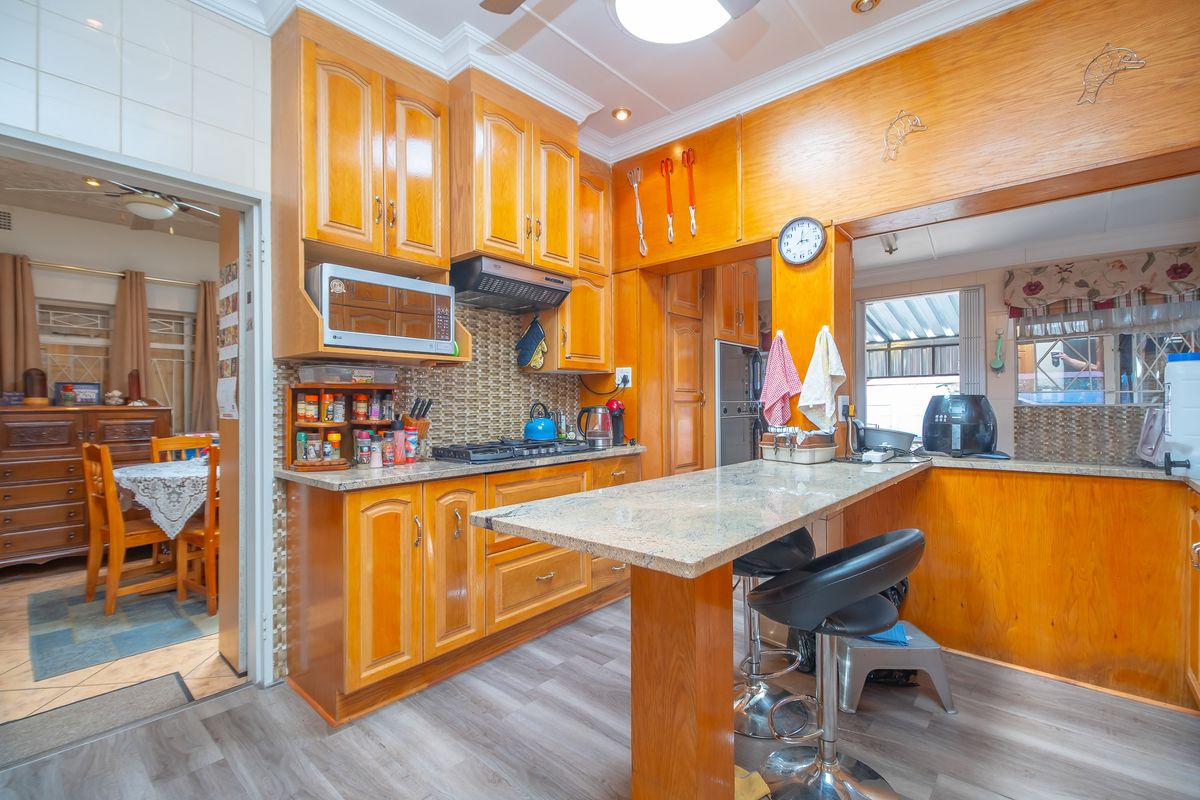 A functional kitchen featuring wood-finish cabinetry, granite countertops, a breakfast bar, and a built-in extractor fan, with an adjacent dining area visible.
