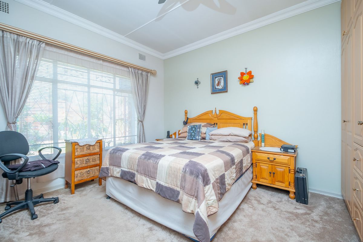 A well-lit bedroom featuring built-in wooden cabinetry, neutral carpeting, and large windows with fitted blinds.