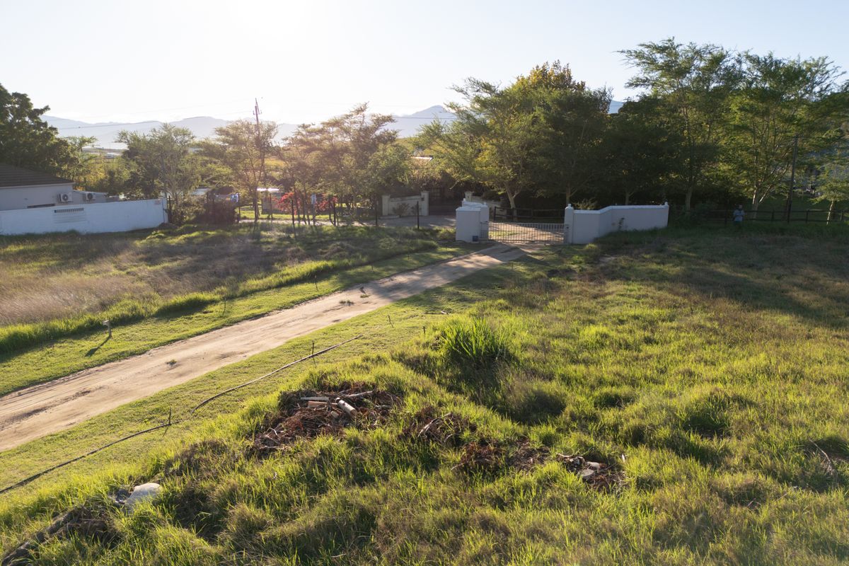An elevated aerial view of a large, undeveloped plot of land featuring a dirt driveway, perimeter walling, and gated entrance.
