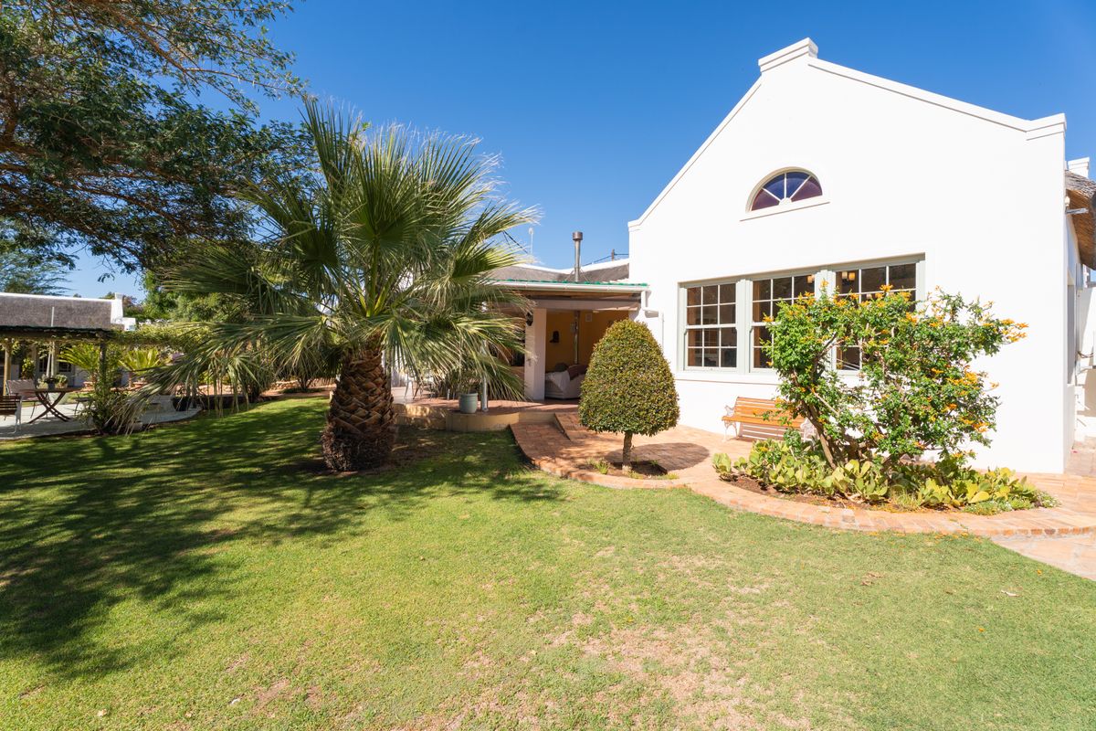 A well-maintained rear garden featuring a brick-paved patio area, lush lawn, and a classic gabled house exterior with multi-pane windows.