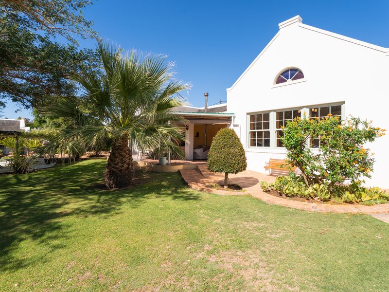 A well-maintained rear garden featuring a brick-paved patio area, lush lawn, and a classic gabled house exterior with multi-pane windows.