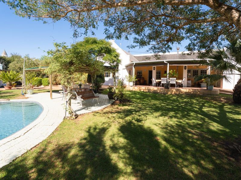 A spacious rear garden featuring a swimming pool, paved surround, and a covered patio area attached to the main residence.