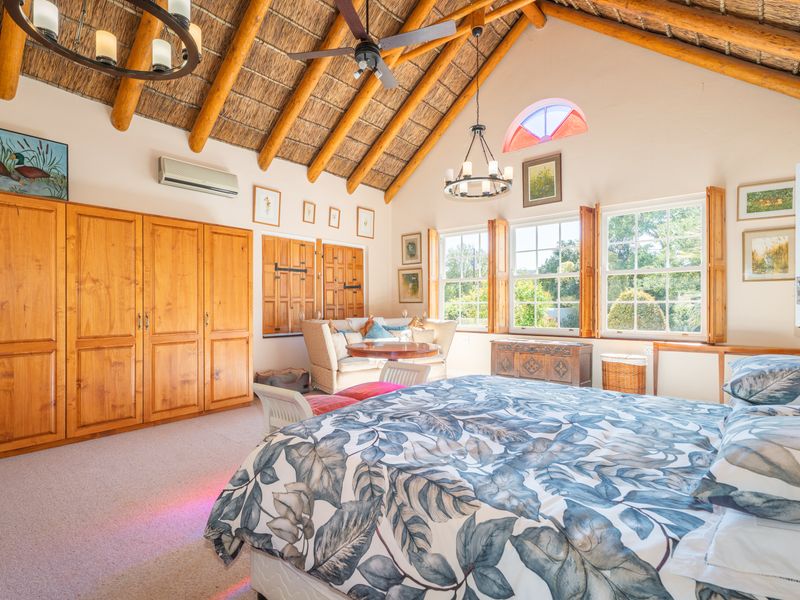 Spacious bedroom featuring high vaulted ceilings with exposed timber rafters, built-in wooden cabinetry, and large windows with timber shutters overlooking the garden.