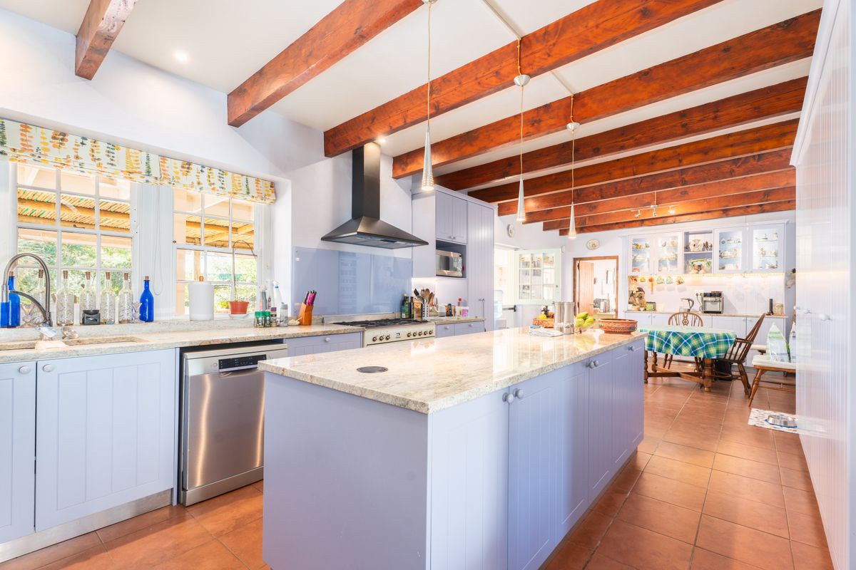 Spacious kitchen featuring a large island with granite countertops, exposed timber ceiling beams, shaker-style cabinetry, and modern integrated appliances.