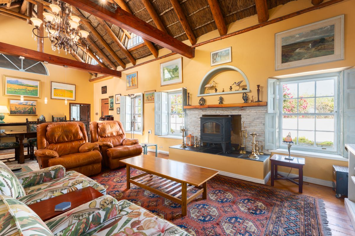Spacious living room featuring a high vaulted thatched ceiling with exposed timber beams, a stone-surround fireplace, and traditional timber window shutters.