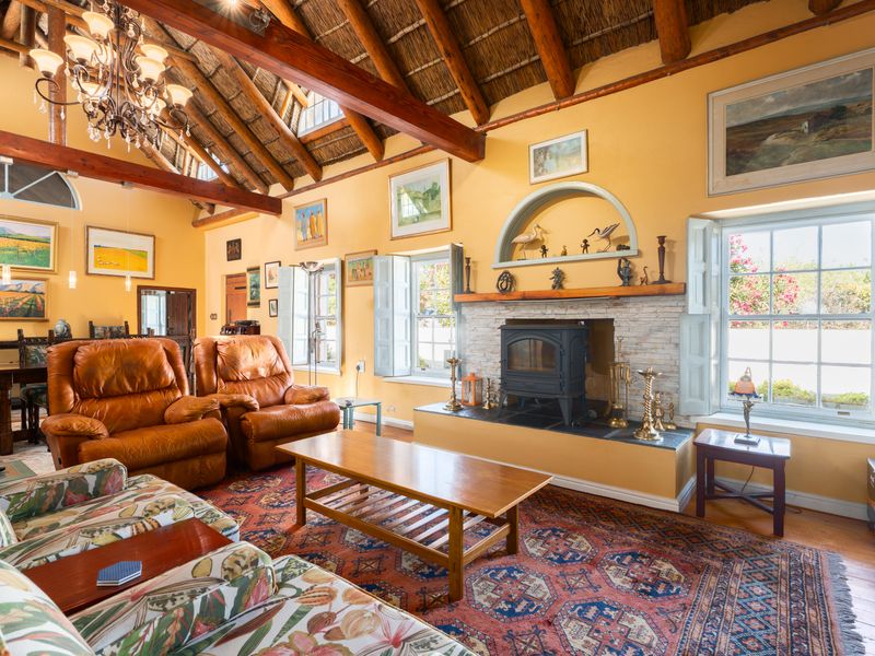 Spacious living room featuring a high vaulted thatched ceiling with exposed timber beams, a stone-surround fireplace, and traditional timber window shutters.