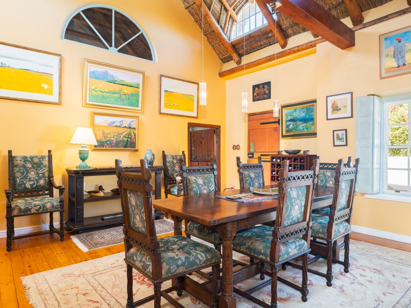 A characterful dining room featuring a high vaulted thatched ceiling with exposed timber beams, warm timber flooring, and an arched feature window.