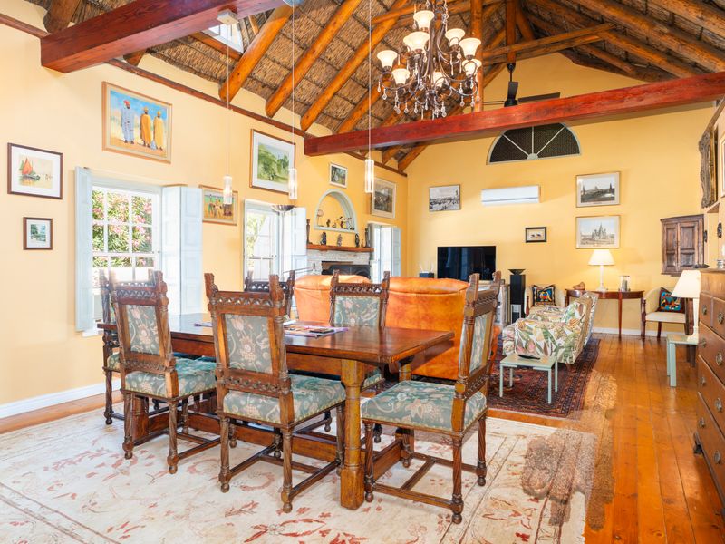 Spacious open-plan living and dining area featuring a high vaulted thatched ceiling with exposed timber beams, hardwood floors, and a built-in fireplace.