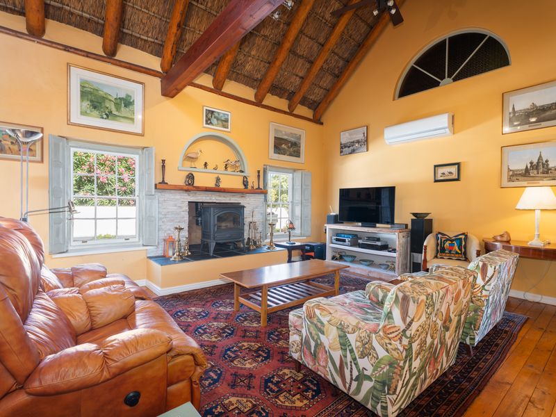 Spacious living room featuring a high vaulted thatched ceiling with exposed timber beams, a cozy cast iron fireplace, and warm timber flooring.