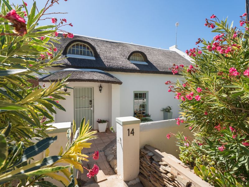 Charming cottage-style home featuring a traditional thatched roof, dormer windows, and a welcoming front entrance with a secure gate and paved walkway.