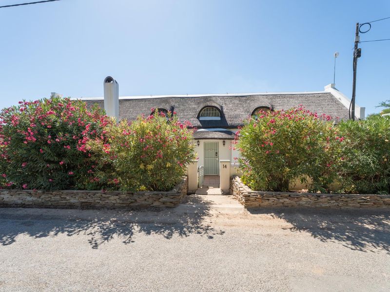 Charming cottage-style home featuring a traditional thatched roof, stone retaining walls, and a welcoming front entrance.