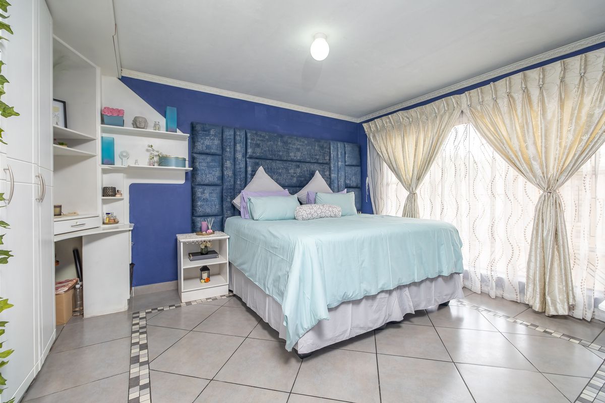 Spacious bedroom featuring built-in shelving, a dedicated vanity area, tiled flooring, and large windows with decorative curtains.