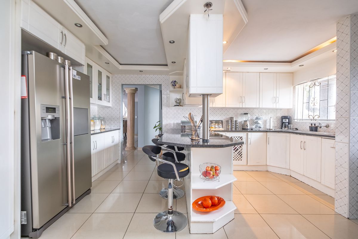 A spacious kitchen featuring white cabinetry, granite countertops, a central breakfast bar, tiled flooring, and recessed lighting.