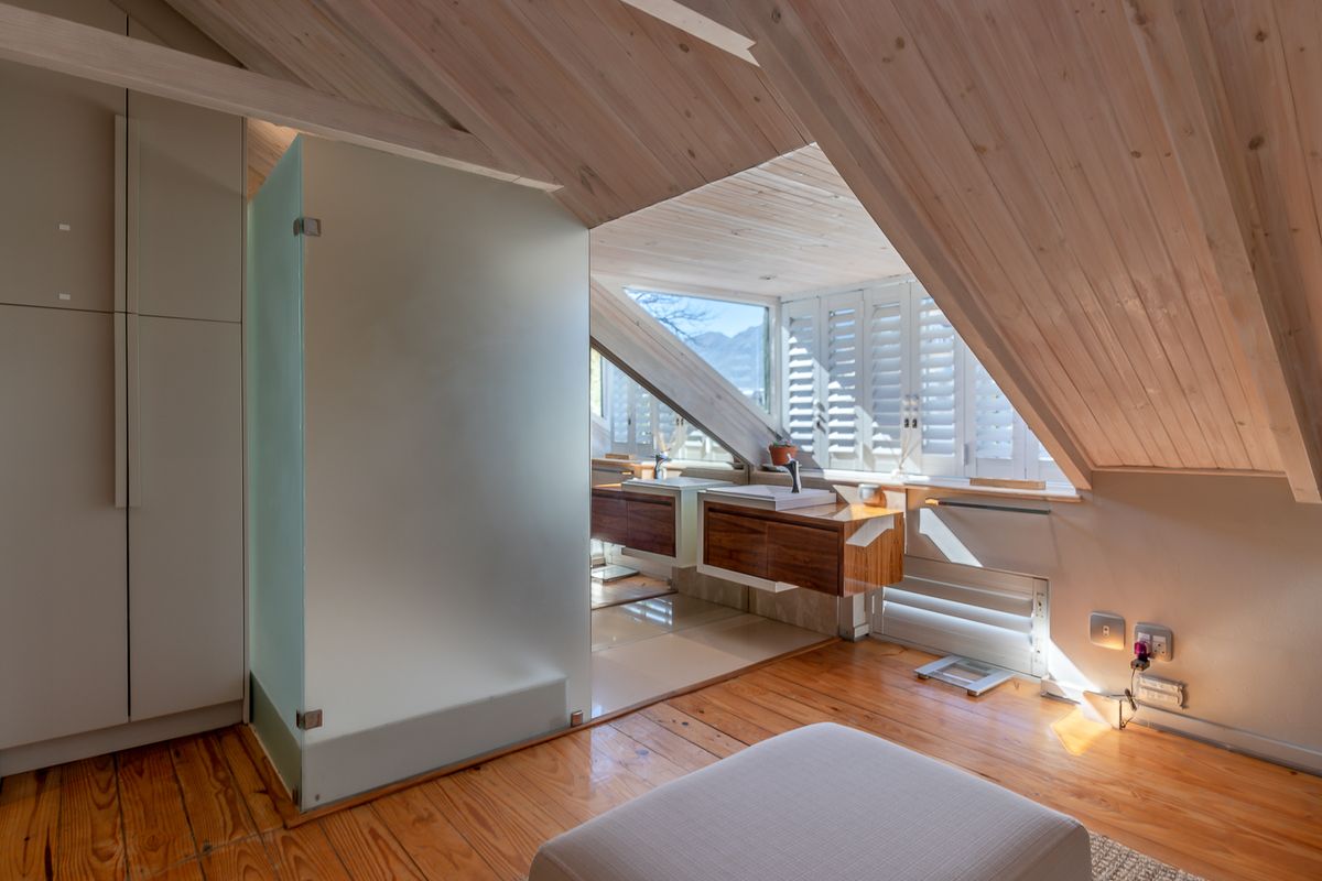 A modern attic-style bathroom featuring timber-clad vaulted ceilings, a floating double vanity, and a frosted glass shower enclosure with natural light.