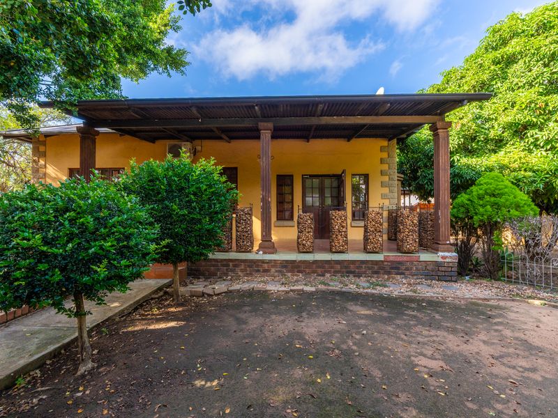 A charming office building exterior featuring a covered veranda with timber columns, brick foundation, and mature surrounding garden landscaping.