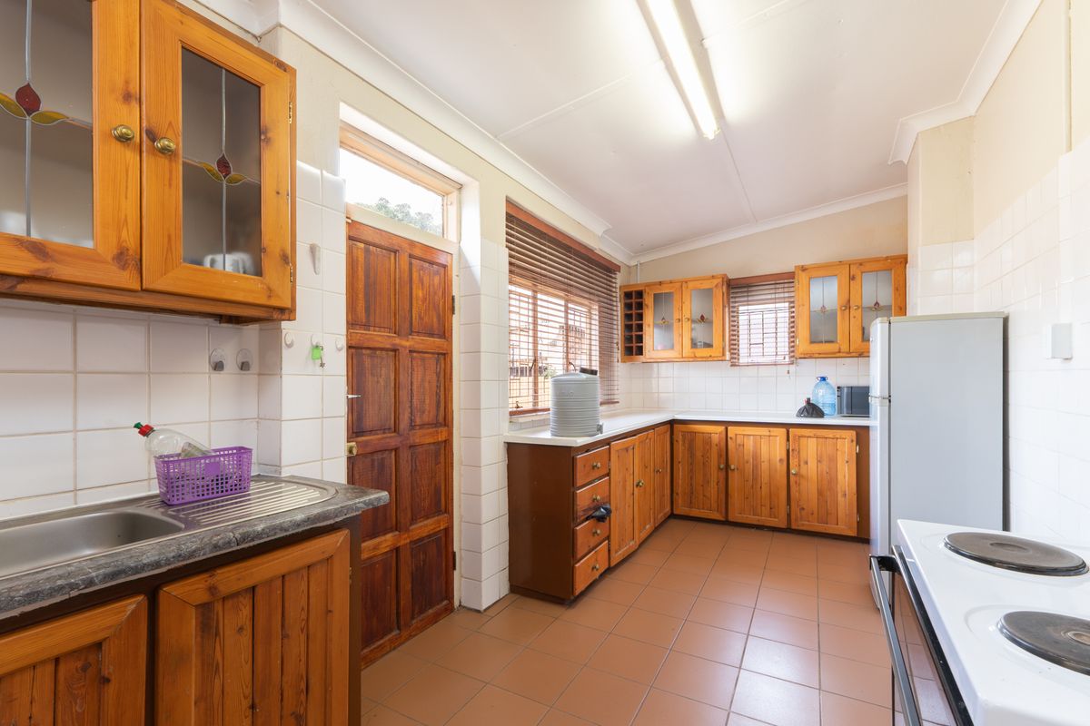 A functional kitchen featuring wooden cabinetry, tiled flooring, and tiled splashbacks, providing a practical workspace with direct exterior access.