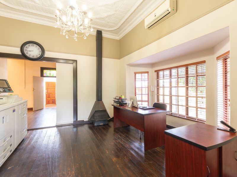 A spacious office area featuring high ceilings with decorative molding, a built-in fireplace, and large windows with wooden blinds.