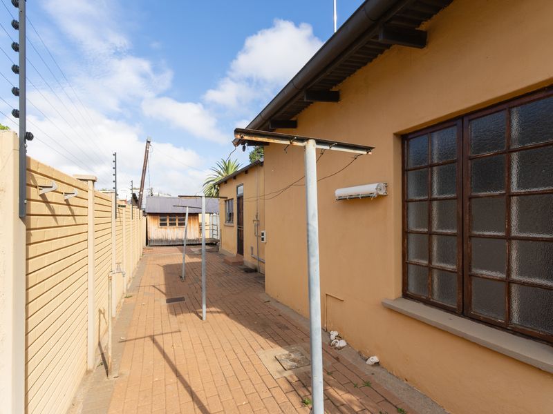 A paved side exterior area featuring a brick boundary wall with electric fencing, metal washing lines, and access to the rear of the office building.