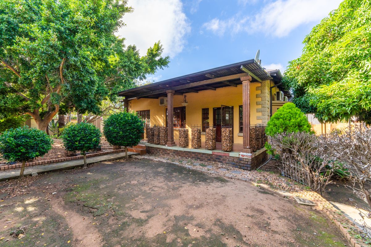 A view of the office property exterior featuring a covered veranda with timber columns, brick base, and surrounding garden area.