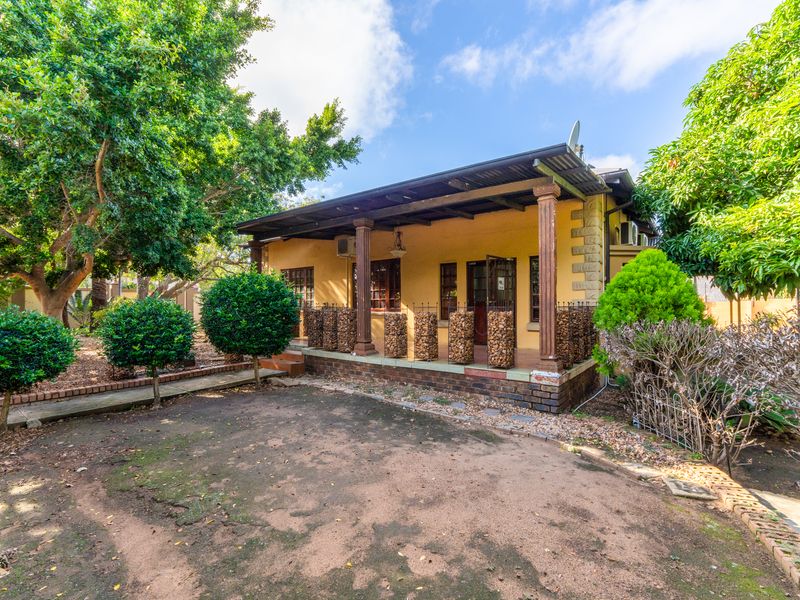 A view of the office property exterior featuring a covered veranda with timber columns, brick base, and surrounding garden area.