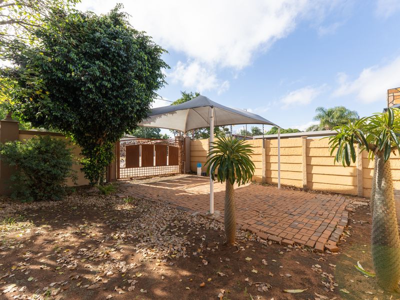 Outdoor paved parking area featuring a shade sail structure, enclosed by a perimeter wall and secure metal gate.