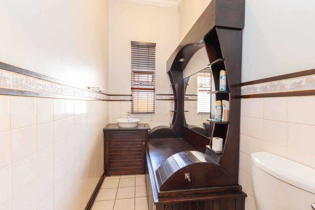 A compact bathroom featuring a vessel sink, built-in vanity, and a toilet, finished with classic wall tiles and a window with blinds.