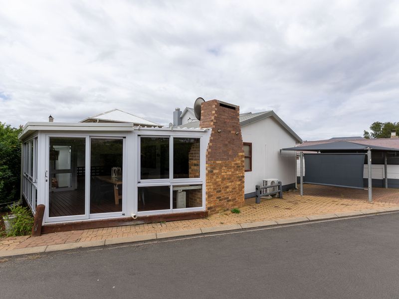 Front exterior view featuring an enclosed patio, brick chimney, paved driveway, and a covered carport area.