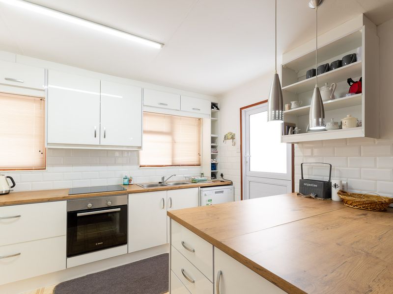 Modern kitchen featuring white cabinetry, wood-look laminate countertops, subway tile backsplash, built-in oven, and electric hob with ample storage and functional workspace.