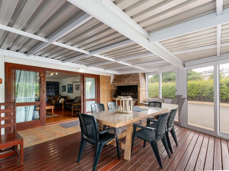 Covered outdoor patio featuring timber decking, a built-in brick braai, and direct access to the interior living area through sliding glass doors.