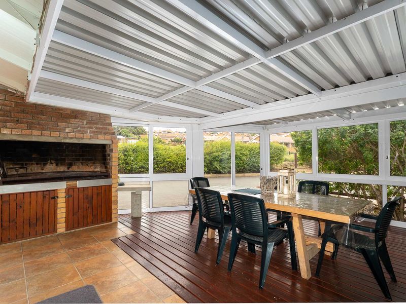 Enclosed patio area featuring a built-in brick braai, timber decking, tiled flooring, and large sliding windows overlooking the garden.