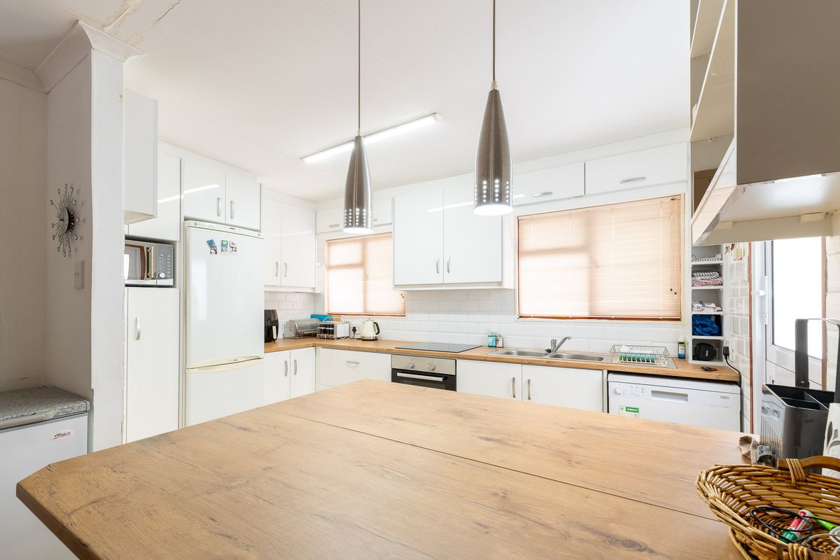 Functional kitchen featuring white cabinetry, subway tile backsplash, timber-look countertops, integrated oven, and cooktop with modern pendant lighting.