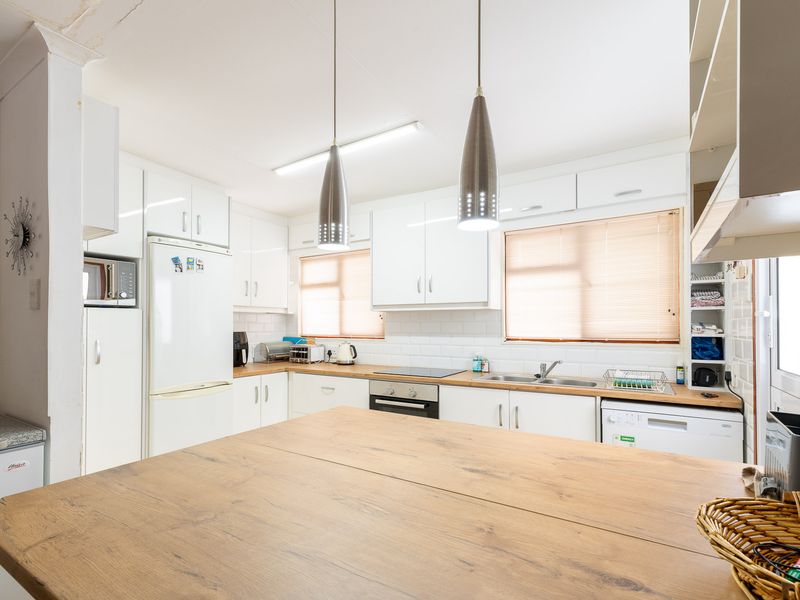 Functional kitchen featuring white cabinetry, subway tile backsplash, timber-look countertops, integrated oven, and cooktop with modern pendant lighting.