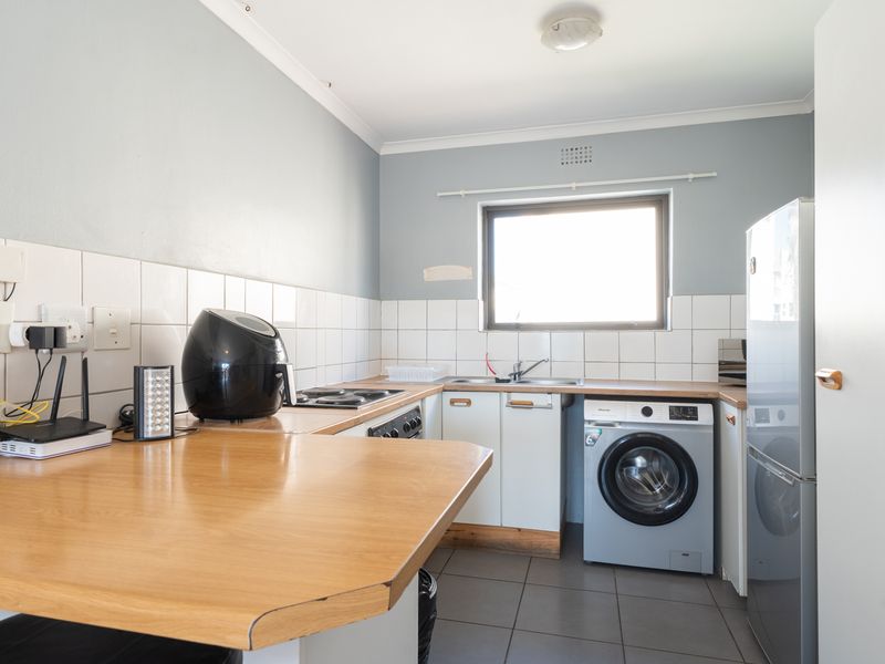 A functional kitchen featuring built-in cabinetry, laminate countertops, tiled backsplash, and integrated laundry plumbing, providing a practical workspace for daily needs.