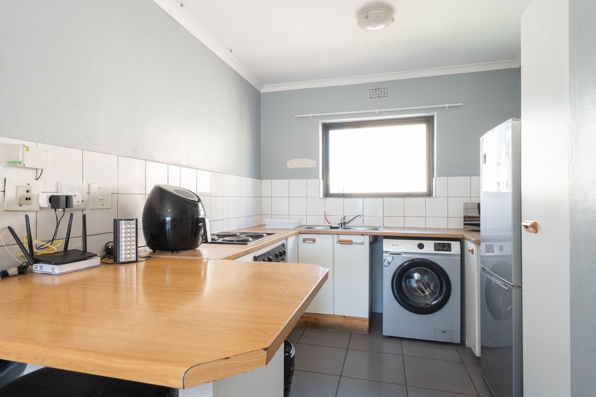 A functional kitchen featuring built-in cabinetry, laminate countertops, tiled backsplash, and integrated laundry plumbing, providing a practical workspace for daily needs.