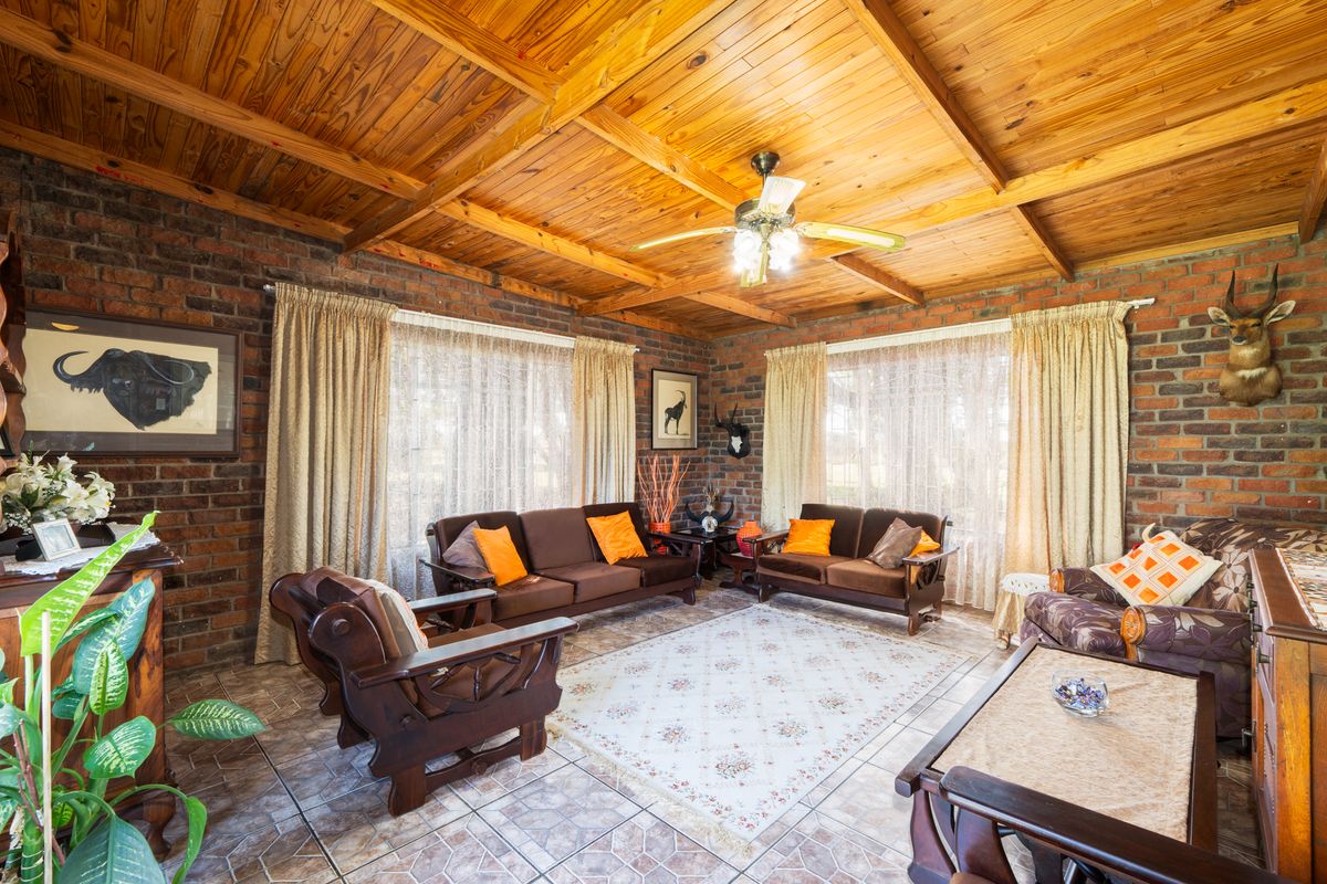 Spacious living room featuring exposed brick walls, a high timber-paneled ceiling with exposed beams, and tiled flooring.
