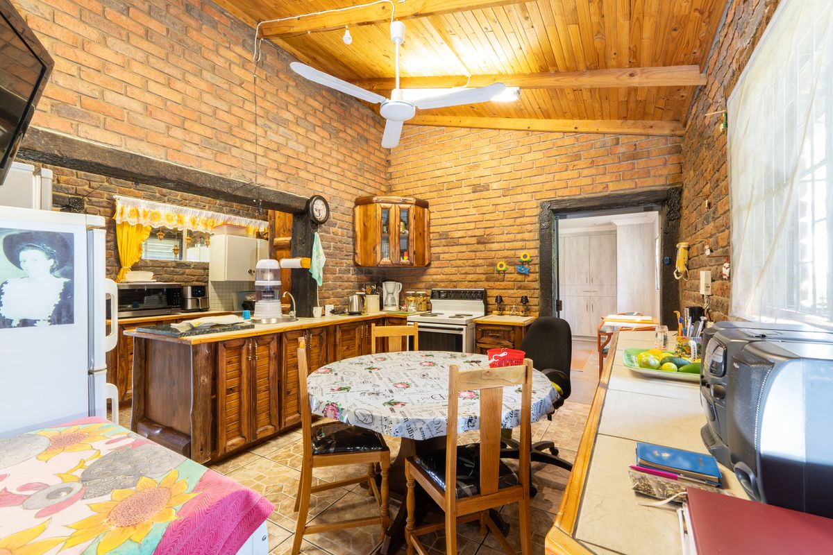 Rustic kitchen featuring exposed brick walls, timber cabinetry, a vaulted wood-paneled ceiling, and a central dining area.