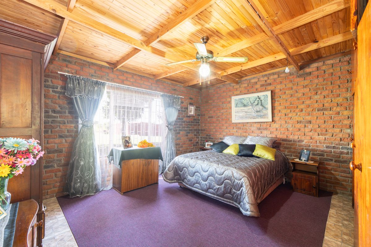 A rustic bedroom featuring exposed face-brick walls, a vaulted timber-clad ceiling with a central fan, and carpeted flooring.