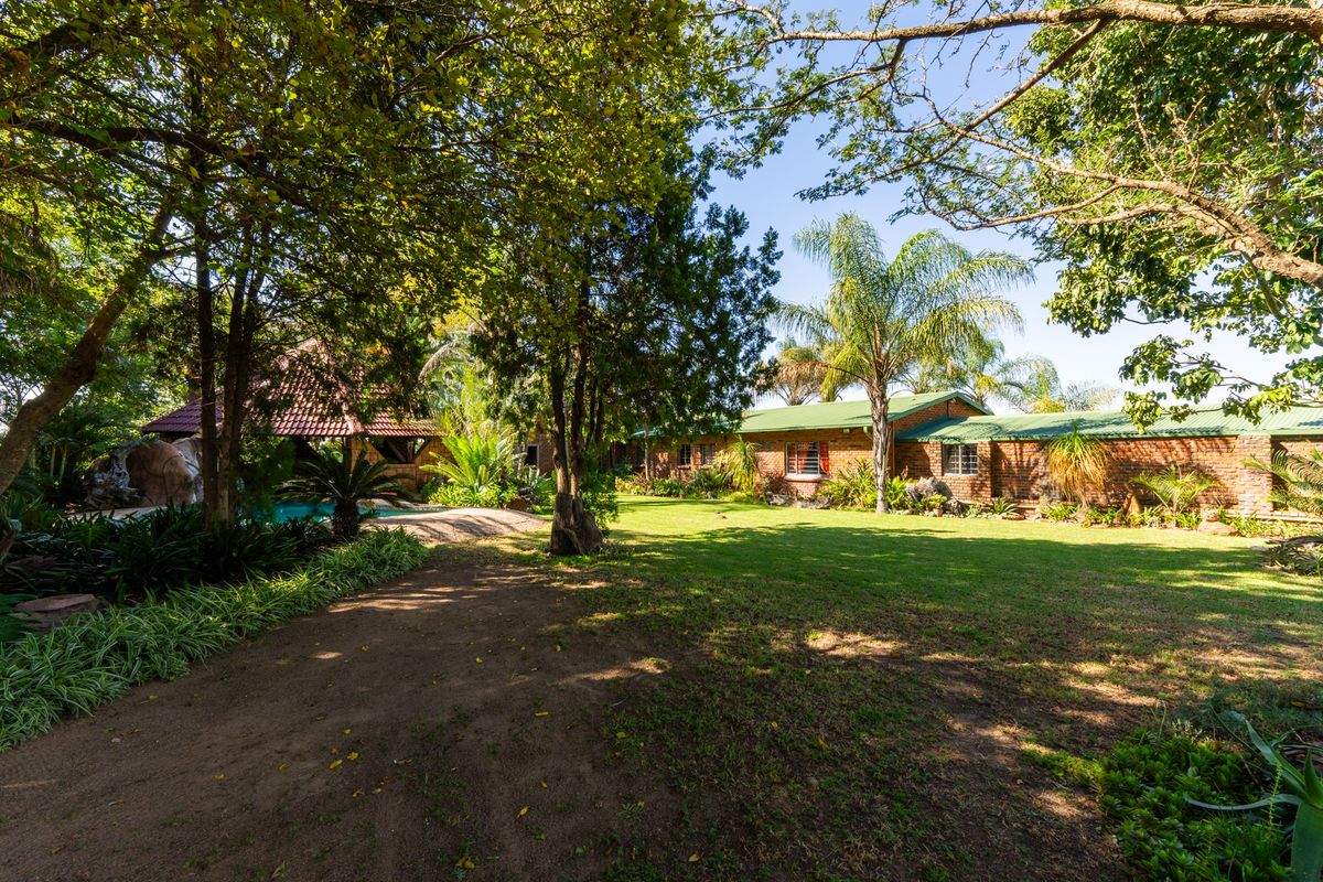 Spacious rear garden featuring a swimming pool, a thatched lapa, and a well-maintained brick farmhouse with a green metal roof.
